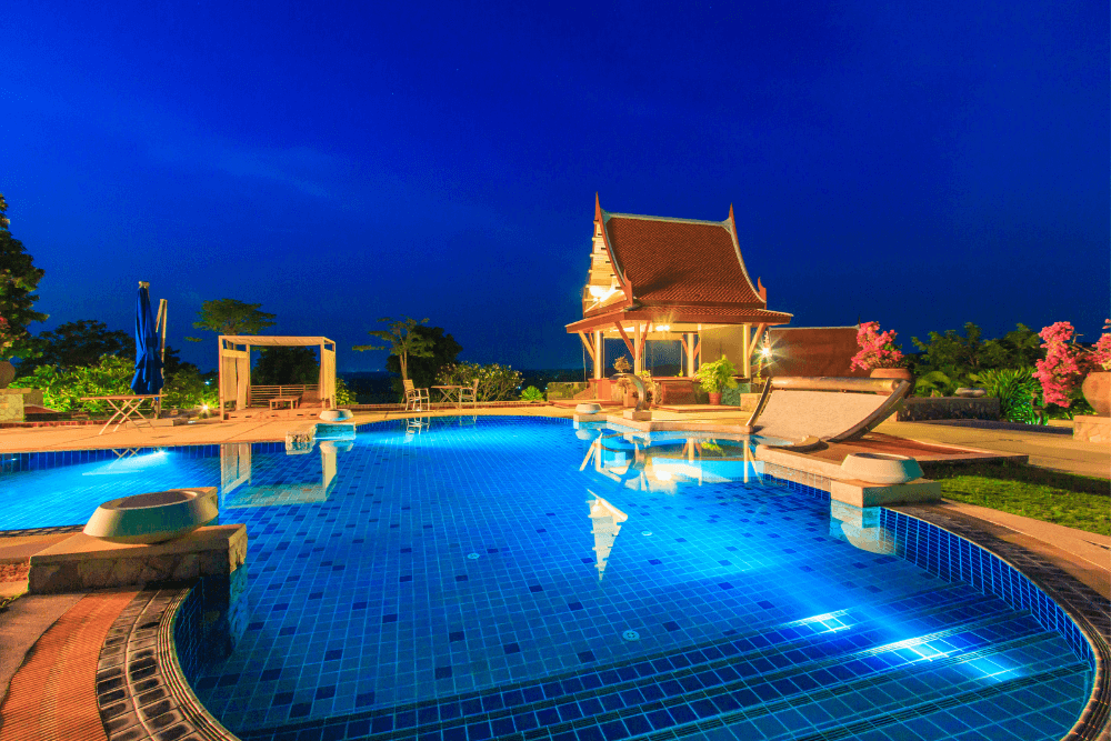 view of a concrete pool deck at night with elegant lighting illuminating the area
